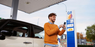 Man standing at a Q8 fuel station holding his smartphone with the Q8 app
