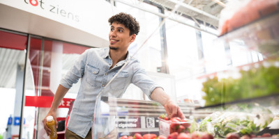 Een man die een pak aarbeien neemt in een Delhaize Shop&Go bij een Q8 tankstation.
