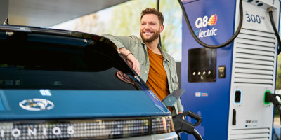 Un homme qui attend que sa voiture soit rechargée à une station de recharge de Q8 electric