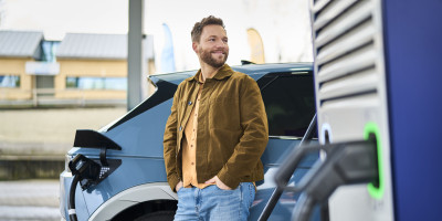 Un homme se tient à côté de sa voiture électrique en train d'être rechargée chez Q8 electric