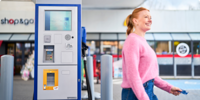 Une femme attend et sourit à la station Q8 electric avec shop&go