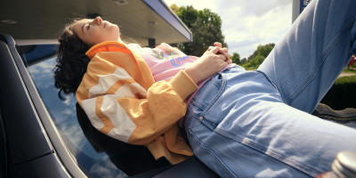vrouw ligt op de voorruit van haar auto met een fles limonade aan Q8 station